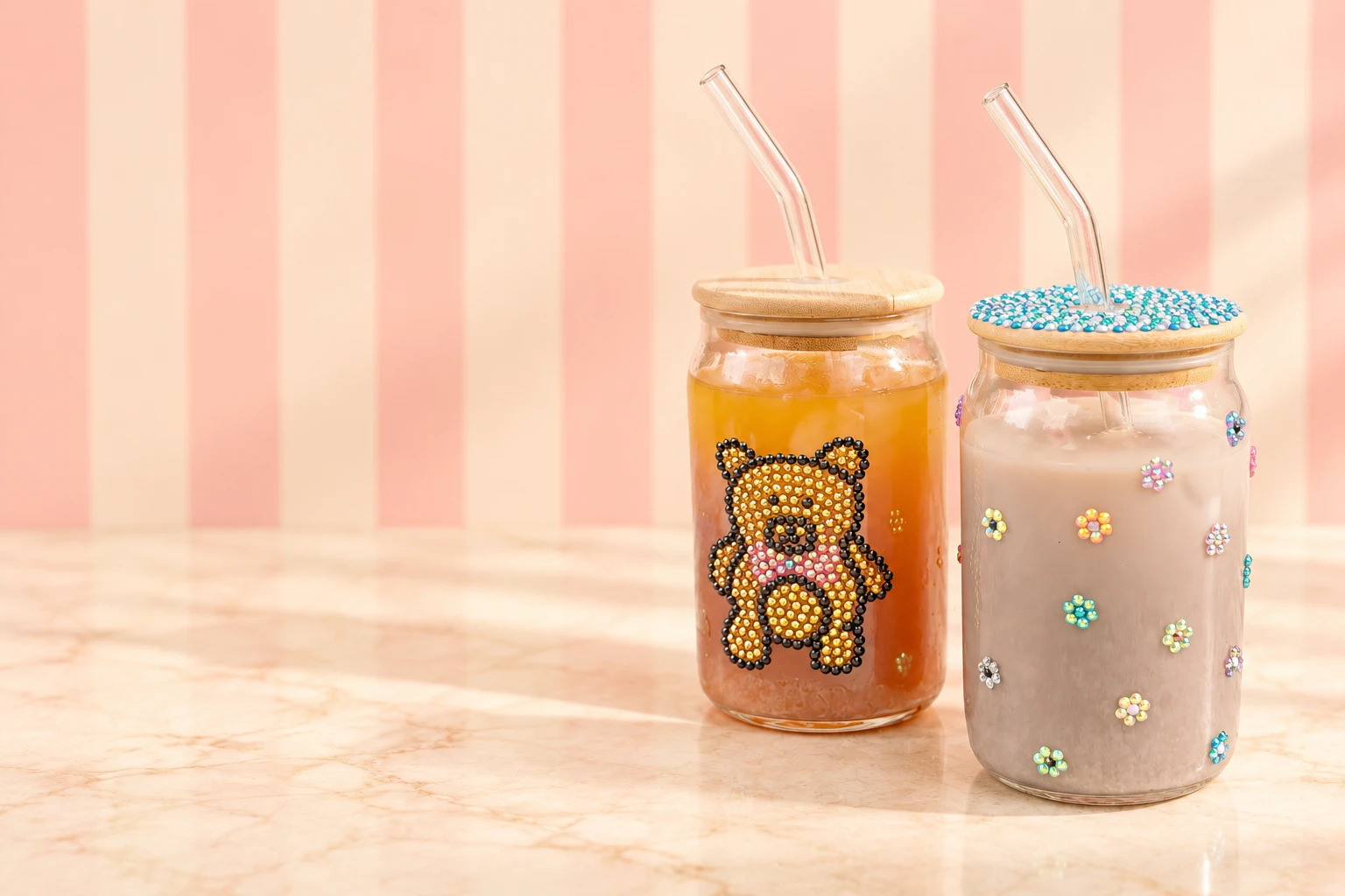 A clear drinking glass decorated with a teddy bear made from rhinestones, beside craft glue, tweezers and loose gems on a cafe table
